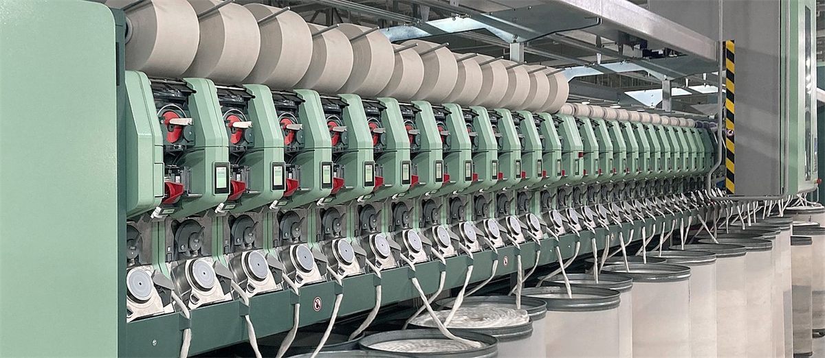 Long row of spinning positions on an open-end rotor-spinning machine, with wound packages above and sliver cans feeding from below